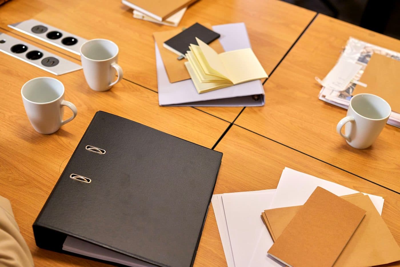 A tidy desk holding a closed binder, loose papers and two coffee cups.