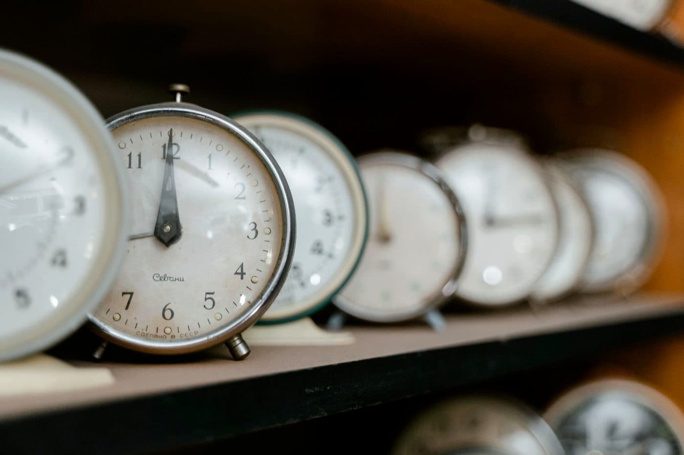 A row of vintage analogue alarm clocks lined up together, each showing a slightly different time.