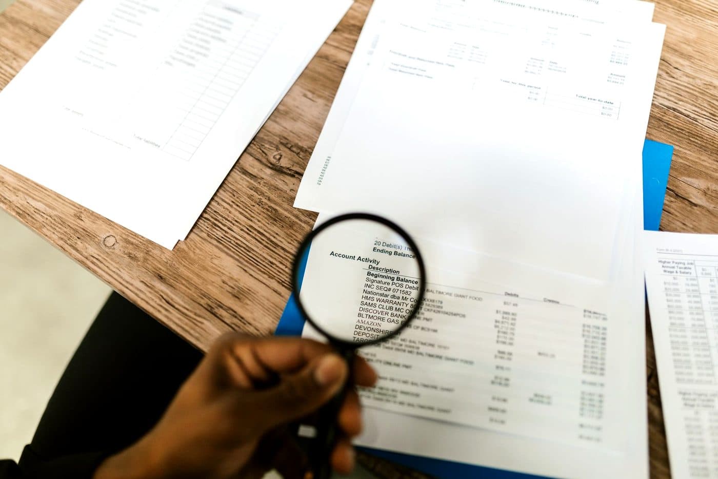 A hand holding a magnifying glass over a printed financial document on a desk.