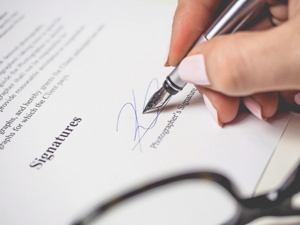 A hand signing a printed document with a fountain pen.