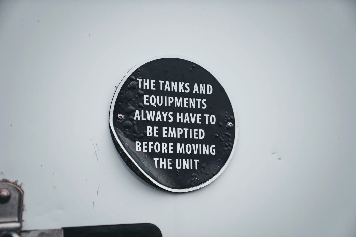 An industrial warning plate reading that tanks and equipment must always be emptied before moving the unit.