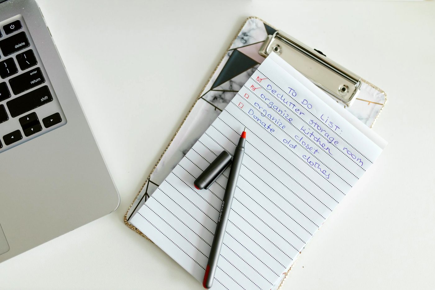 A clipboard holding a handwritten checklist beside a laptop on a desk.