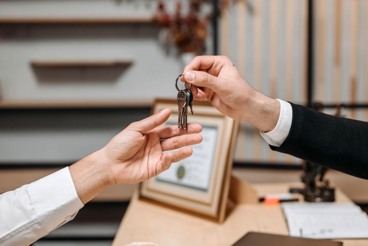 Two people at a desk, one passing a set of keys into the other's open hand.