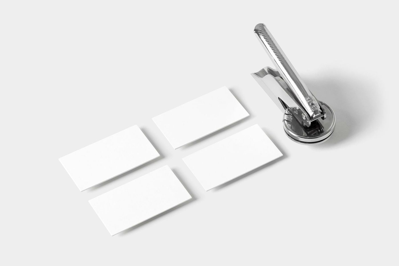 A metal hand embosser beside blank cards on a pale surface.