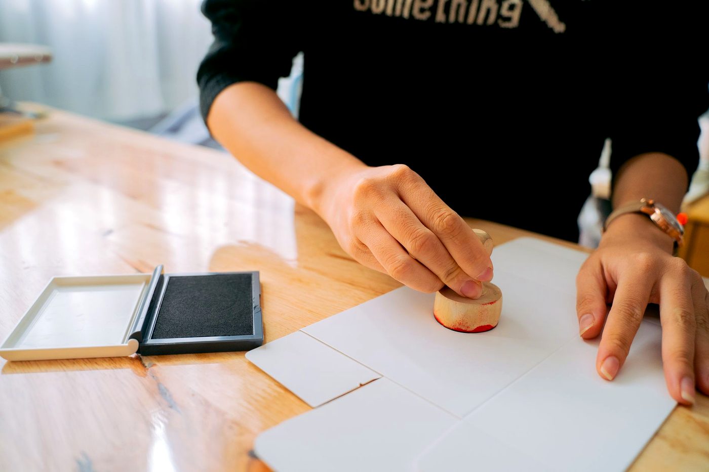 Two hands applying a rubber stamp to a document on a desk.