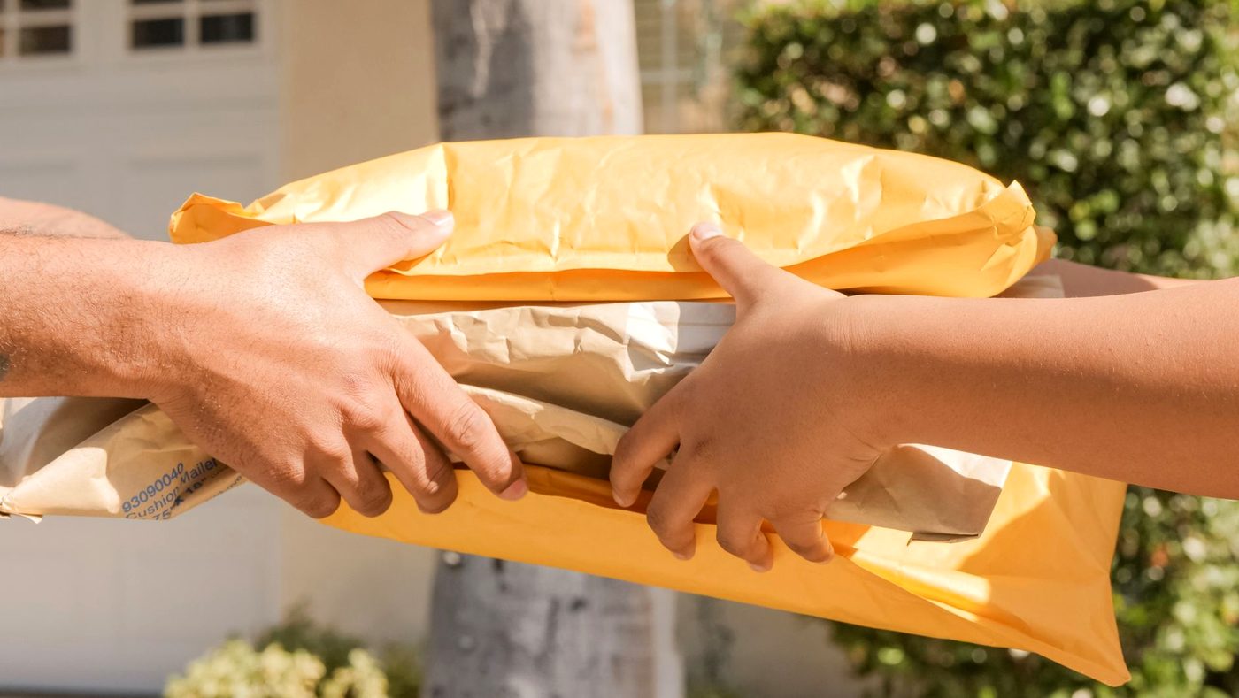 A padded envelope passing between two people's hands.