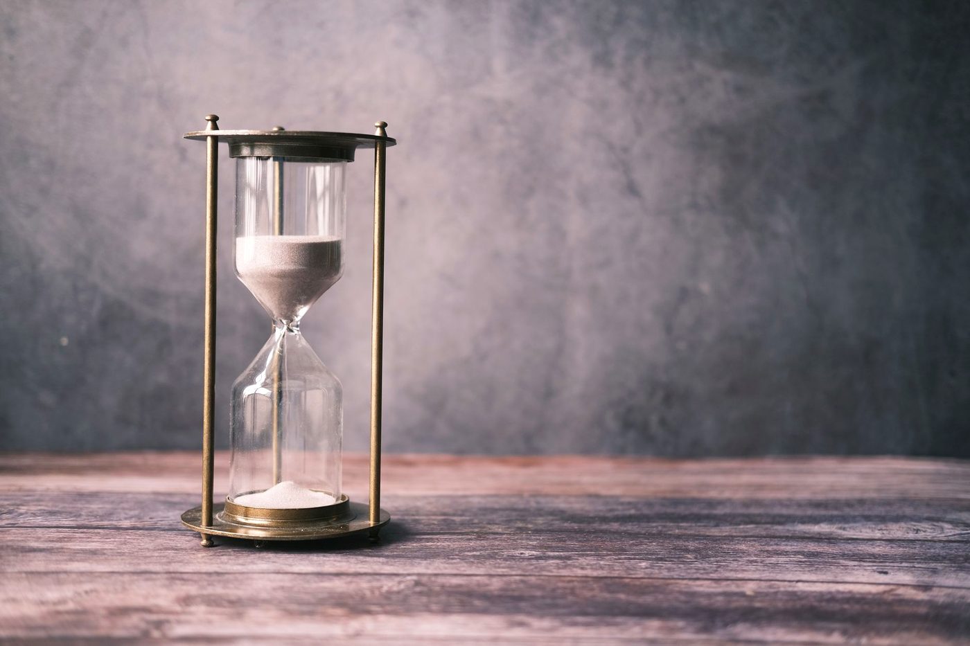 A classic hourglass with sand running through it, resting on a rustic wooden surface.